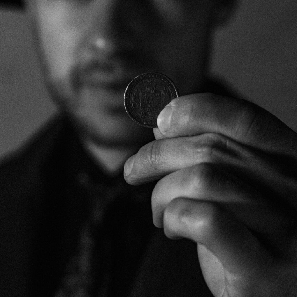 A man holds a coin close to the camera in a dramatic black and white image.
